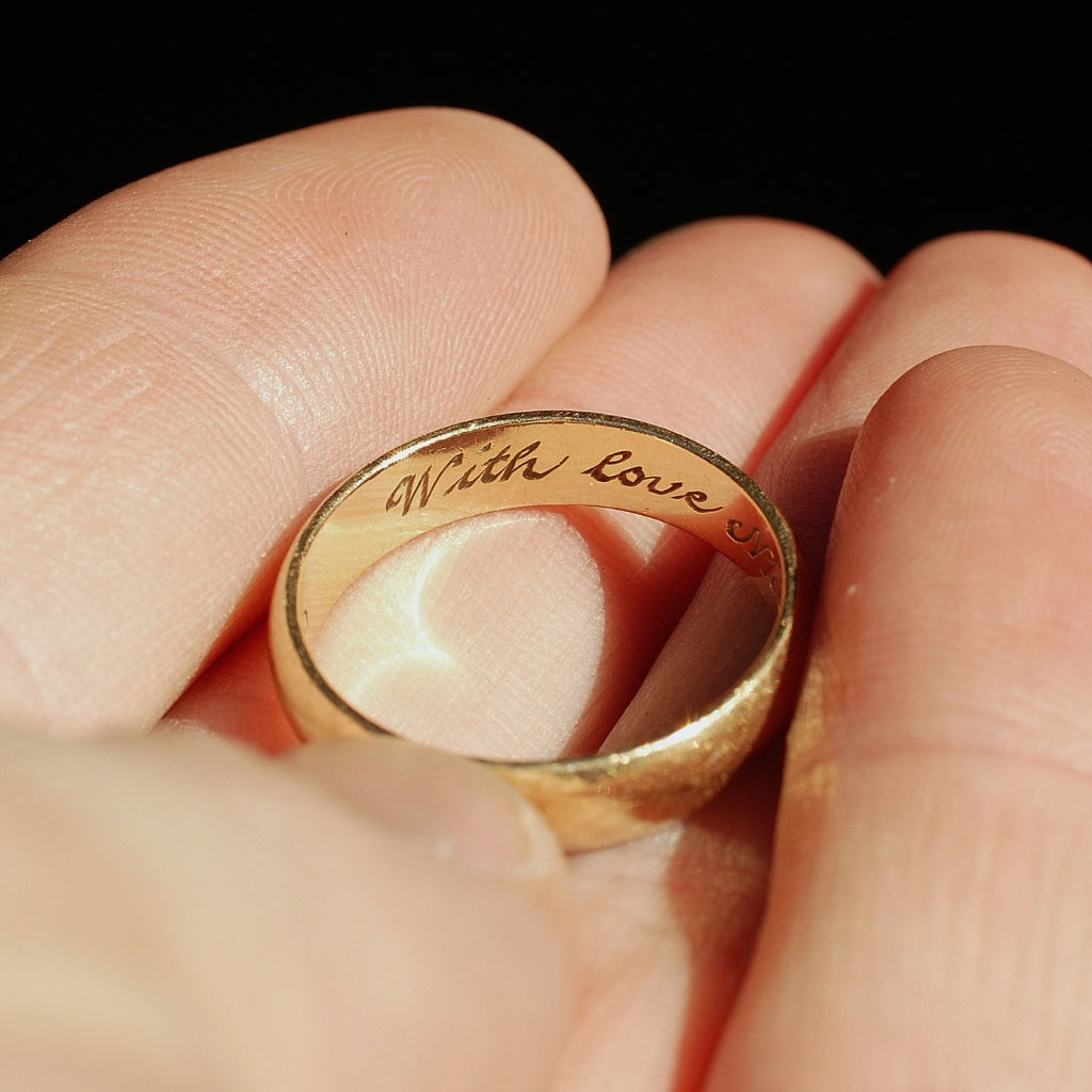 Gold ring with 'With Love' engraving on a finger against a dark background