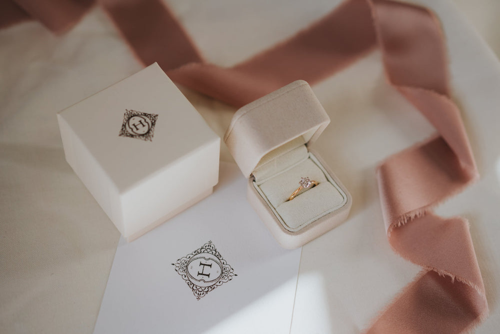 Ring in an open jewelry box with a pink ribbon on a matching box