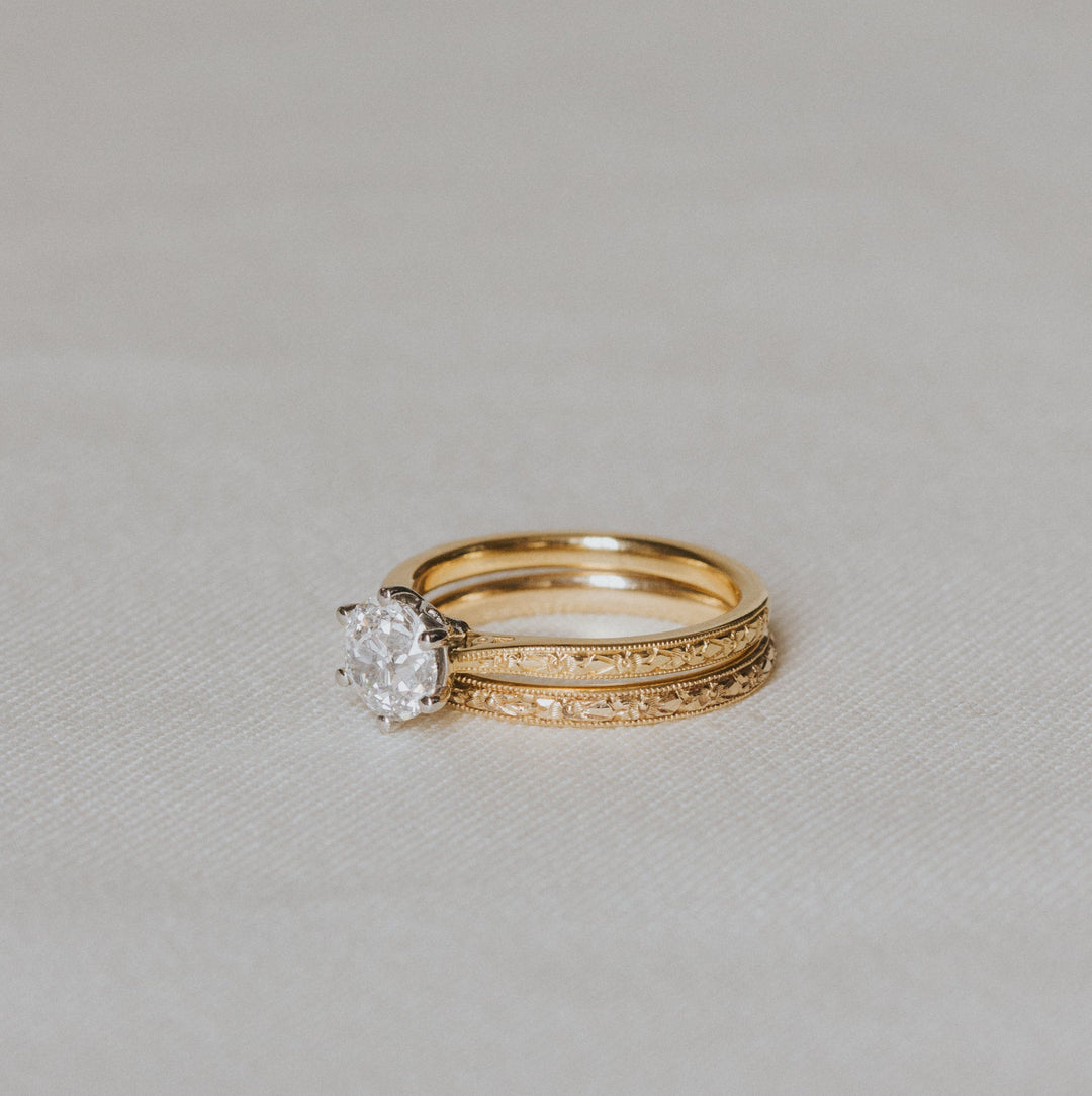 Gold engraved ring with a diamond on a light gray background